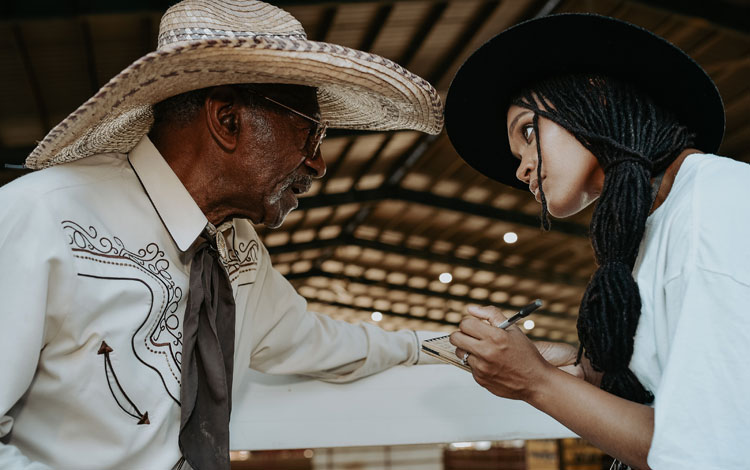 A woman holding a notepad interviewing a cowboy, BPIR contestant Adam Ezell Jr.